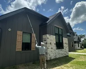 Technician using a long extension pole to reach the eaves of a modern dark-gray house.
