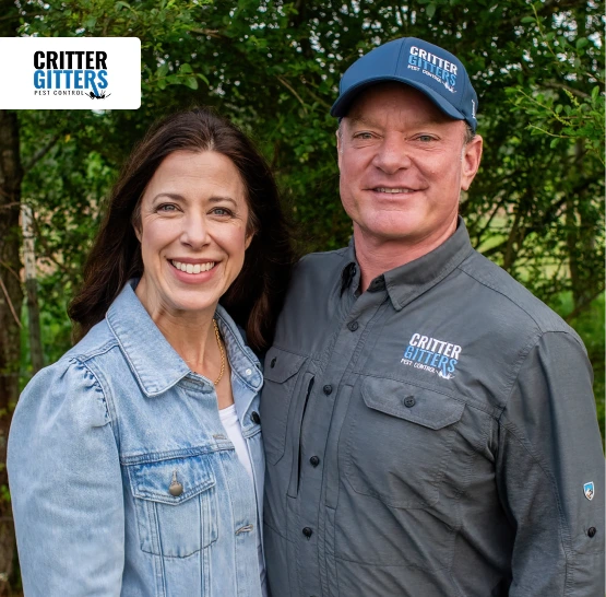 Smiling man and woman in Critter Gitters branded attire standing in front of greenery.