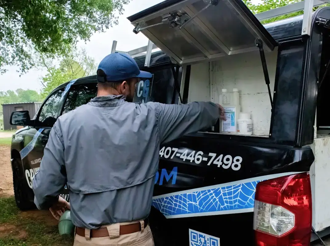Pest control technician retrieving supplies from a black service truck compartment